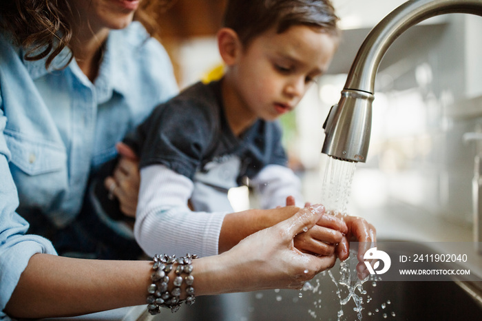 Midsection of mother assisting son in washing hands at home