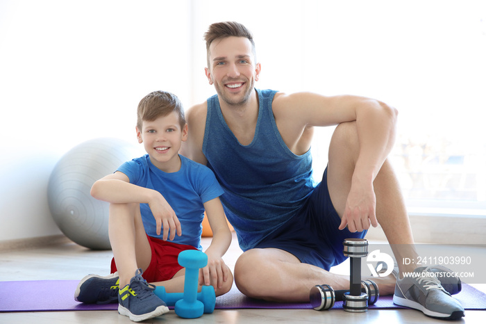 爸爸和儿子在健身房拿着哑铃坐在地板上