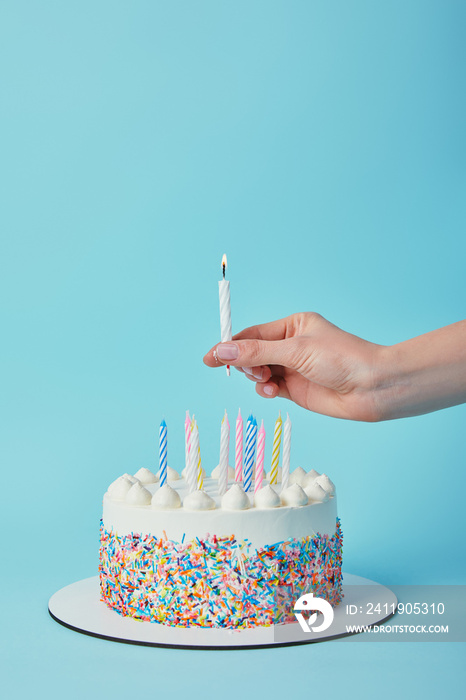 蓝色背景下一名妇女在生日蛋糕上点燃蜡烛的局部视图