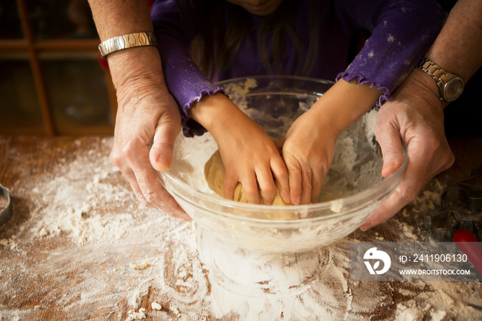 Close up of grandmother kneading dough with granddaughter