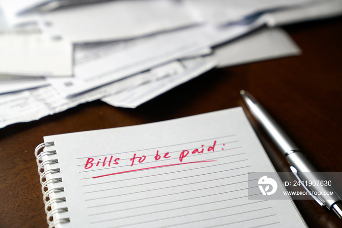 Bills to be paid, red color written words on notebook with bills and invoices at the background