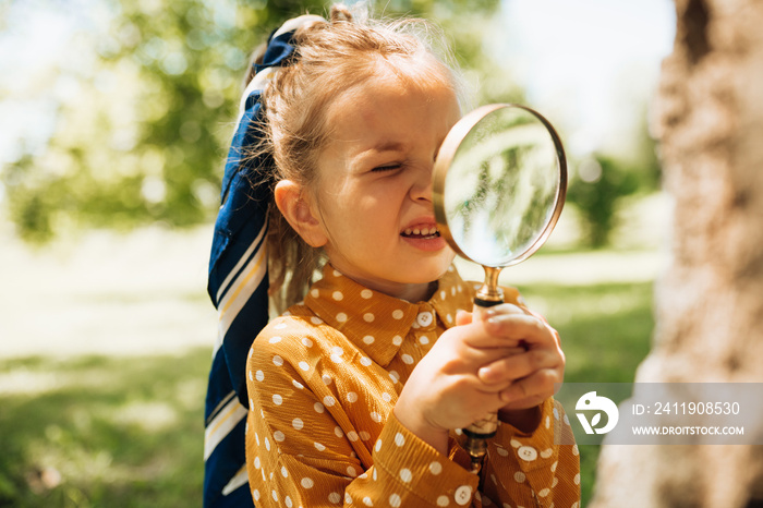 Portrait of cute little girl learning and exploring the nature with magnifying glass outdoors. Child