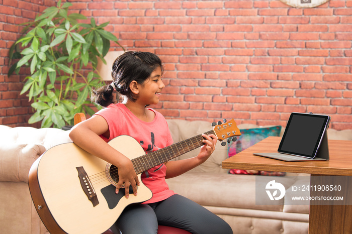 Asian Indian cute little girl learning music at home attending online class on laptop or tablet pc