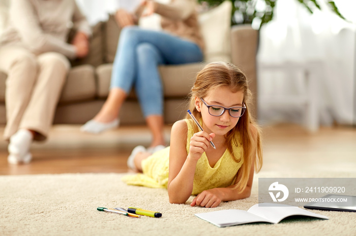 education, school and learning concept - student girl lying on floor and writing to notebook at home