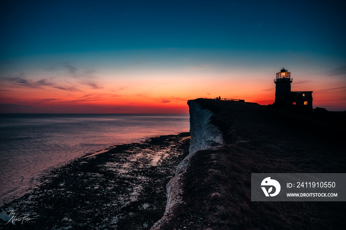 Sunset on edge of cliffs with lighthouse in the back and ocean - sea on horizon