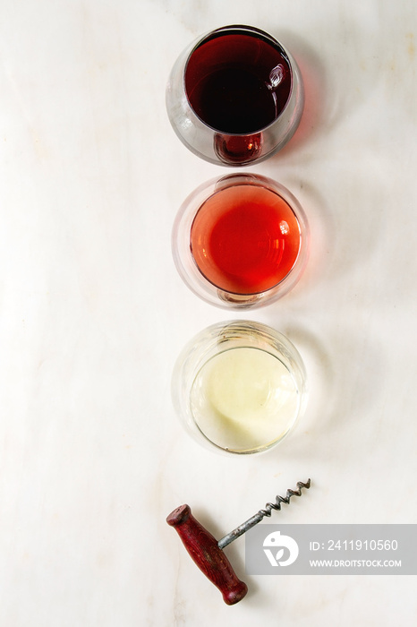 Variety of wine. Red, rose and white wine in old fashion glasses with vintage corkscrew. White marbl