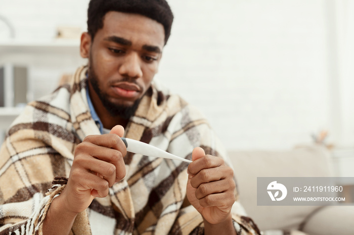 African-american man checking his body temperature at home