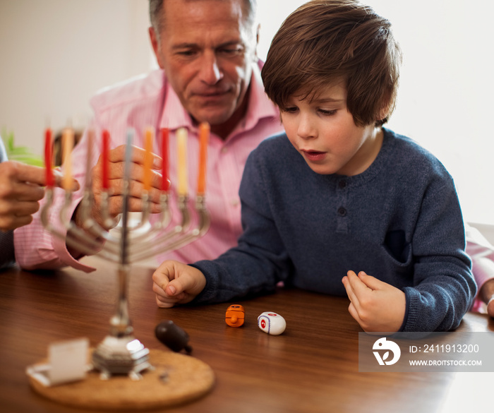 光明节期间，祖父看着孙子在桌子上玩dreidel