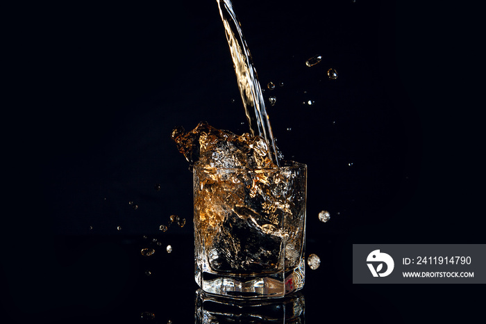 Whiskey pouring into glass with ice isolated on black background..