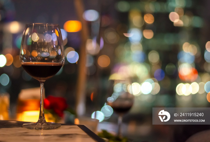 屋顶酒吧桌子上的一杯红酒，有五颜六色的城市灯光和文字空间。