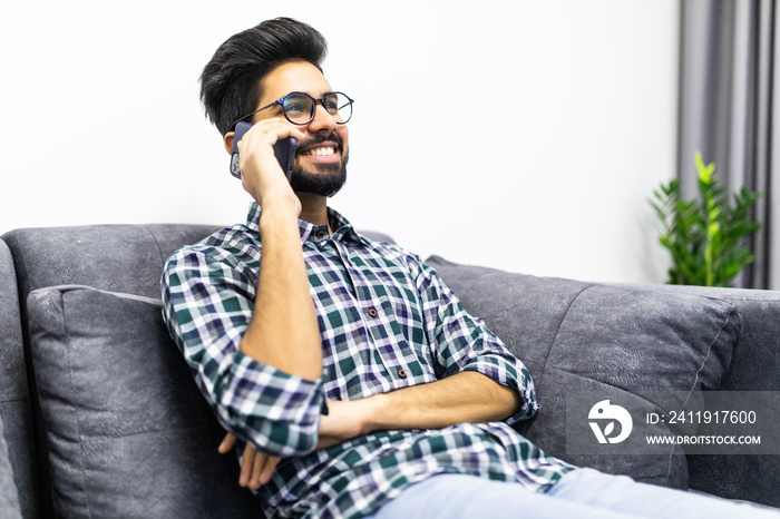 Young indian man talking on the phone while sitting on a couch