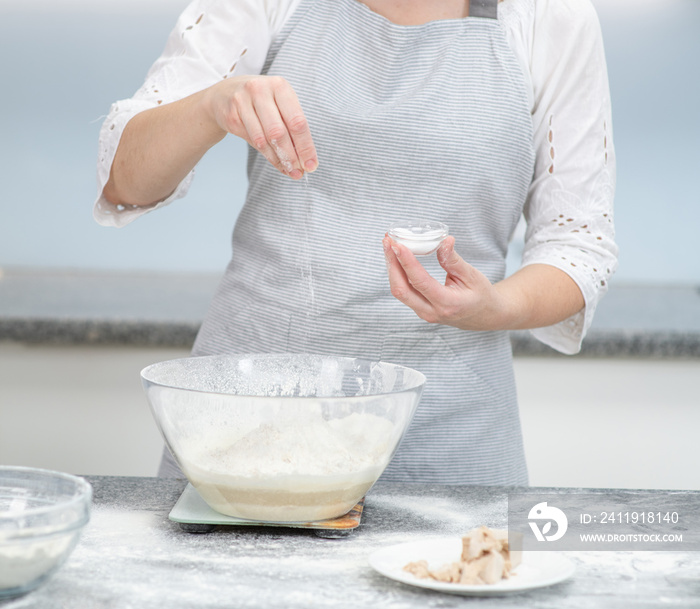 Woman pours salt into the dough at kitchen