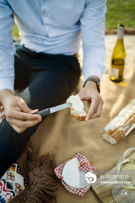 Midsection of man spreading cheese on bread while sitting in park