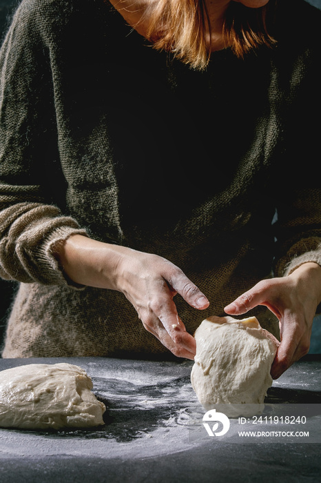 Process of making homemade bread dough. Female hands splits dough on dark kitchen. Black table with 