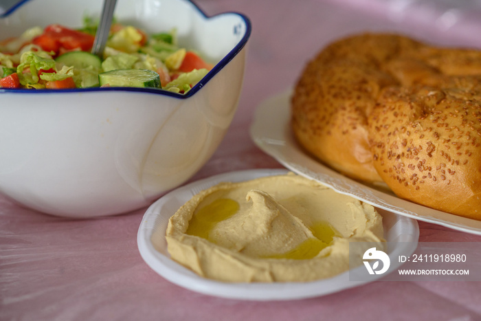 Challah bread on a table for Shabbat meal and traditional homemade hummus, served with salad on pink