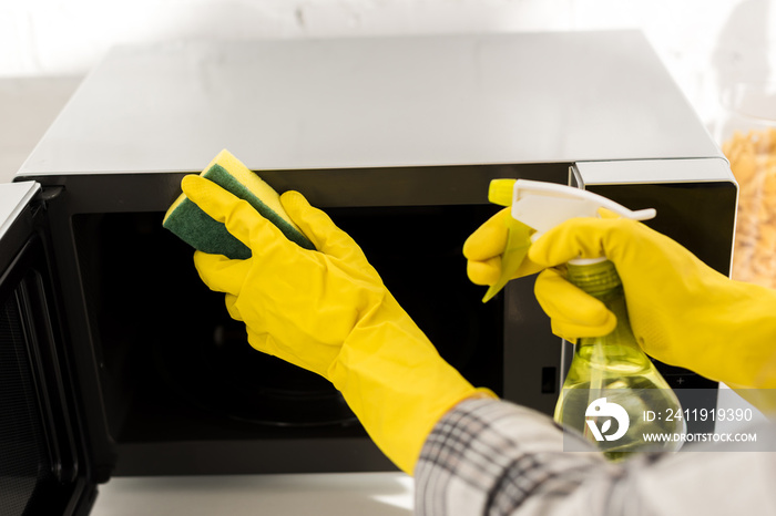 戴橡胶手套的妇女用海绵清洁微波炉的裁剪视图