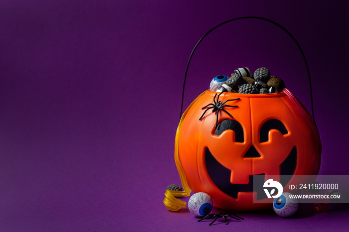 Jack-o-lantern bag full of candy on a purple background with copy space, horizontal