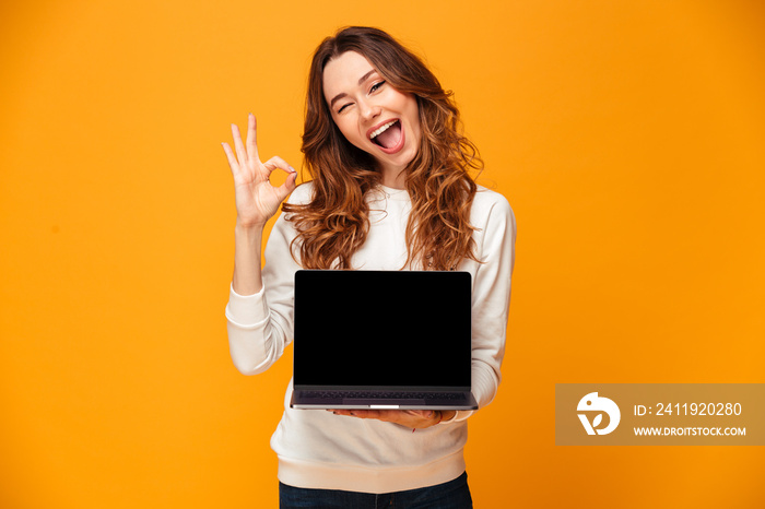 穿着毛衣的快乐深色女人展示笔记本电脑的空白屏幕