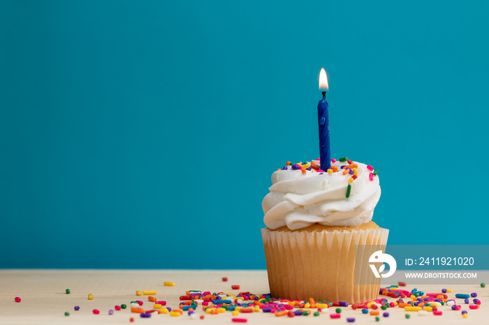 Yellow Cupcake with candle and sprinkles on a blue background, with room for text