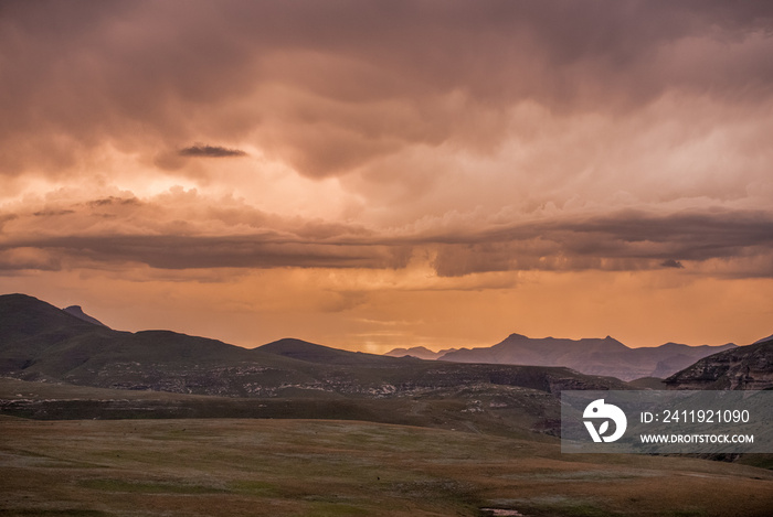 Storm clouds lit up in dramatic colours at sunset over the Drakensberg mountains surrounding the Amp
