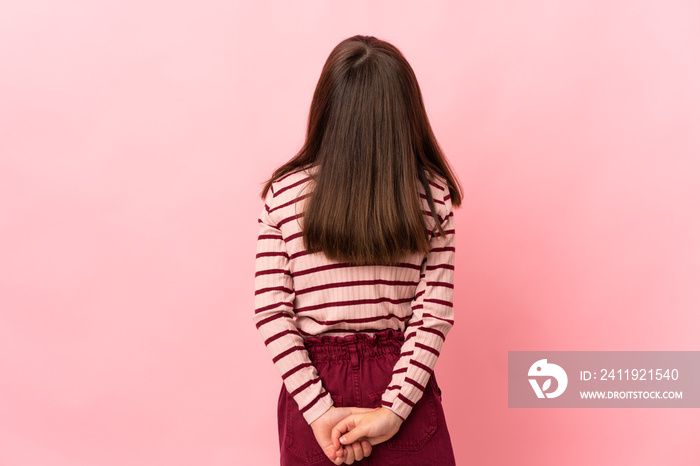 Little girl isolated on pink background in back position and looking back