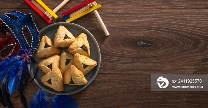 Carnival attributes and тraditional jewish sweets hamantaschen cookies in a plate on a wooden backgr