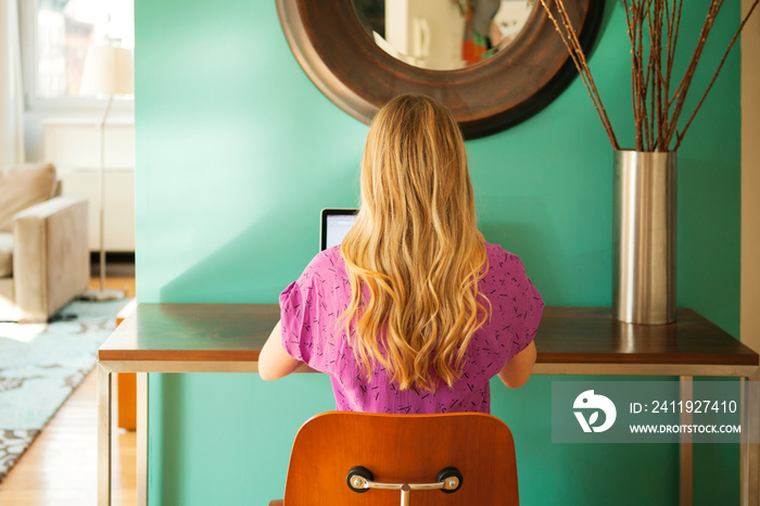 Rear view of blond woman working on laptop at home