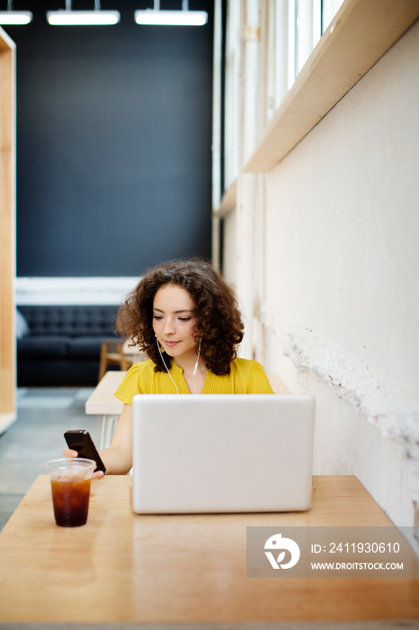 Young woman using mobile phone and laptop at table in cafe