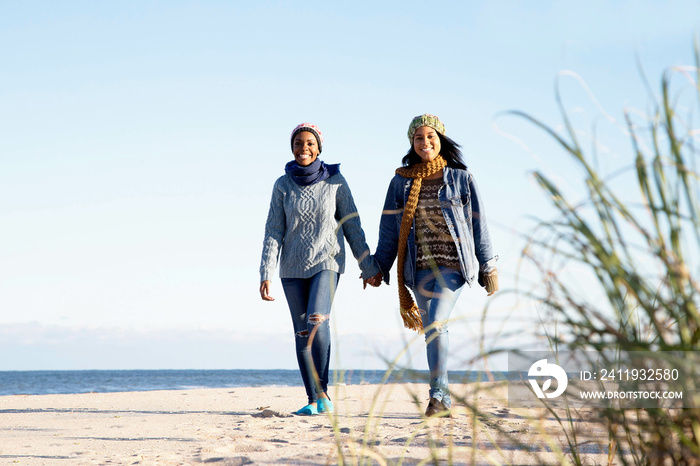 Two young women, walking along beach, holding hands, smiling