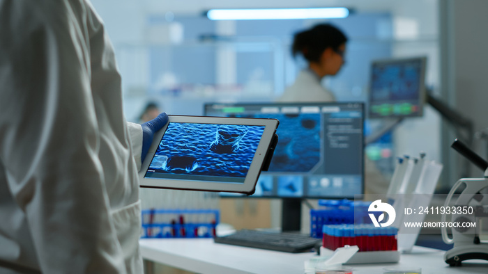 Close up of scientist in lab coat working holding tablet standing in modern equipped laboratory. Tea