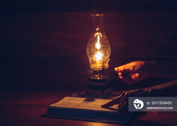 Close up of woman hands hold oil lamp while reading bible in the dark room, Christian background dev