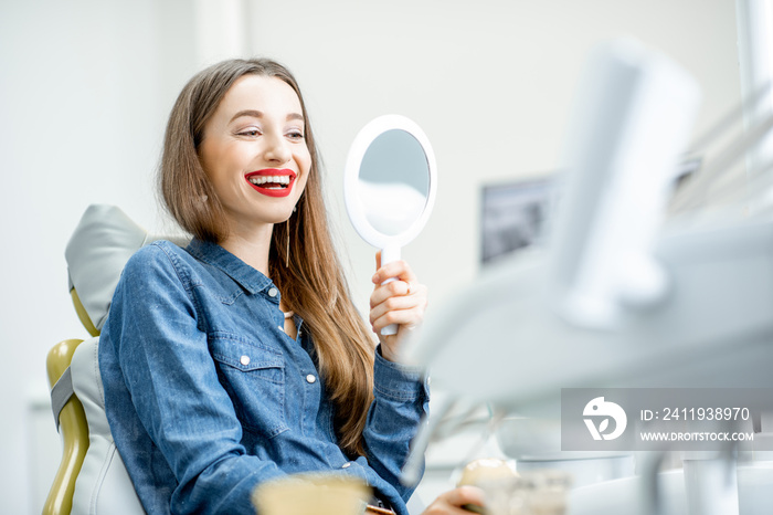 Portrait of a young beautiful woman looking on the mirror enjoying her beautiful smile in the dental