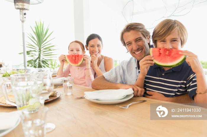 Portrait playful family with watermelon smiles at table