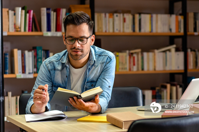 Young male student study in the library reading book.