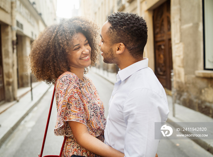 Side view of happy loving couple talking while standing on street amidst buildings in city