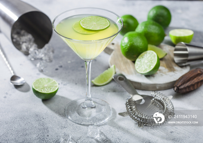 Gimlet Kamikaze cocktail in martini glass with lime slice and ice on light board with fresh limes an