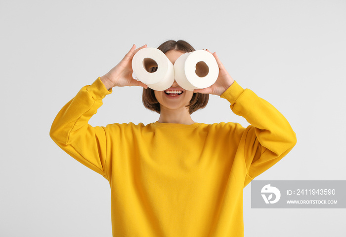 Funny young woman with toilet paper on light background