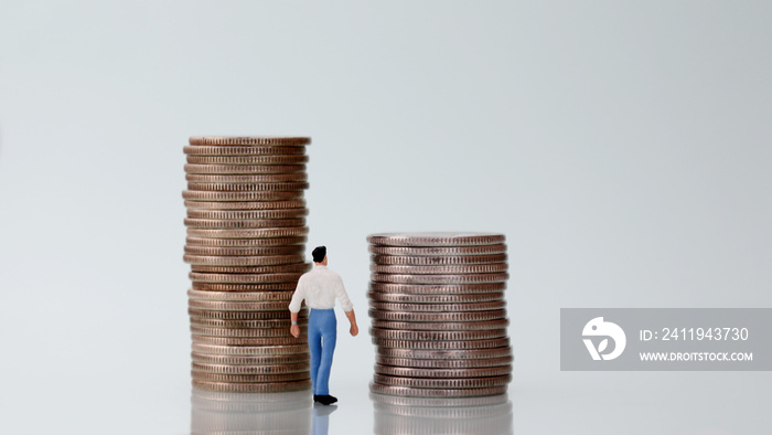 The back of a miniature man watching two pile of coins.