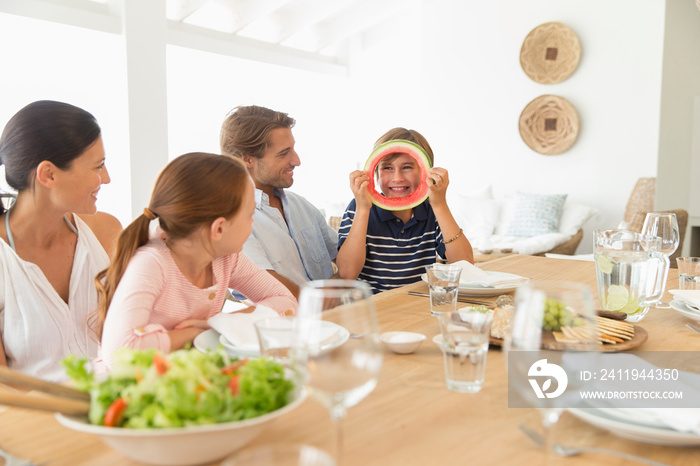 Playful boy with watermelon ring at table with family