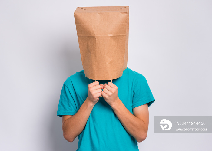 Portrait of teen boy with paper bag over head. Teenager cover head with bag holding hand near face p