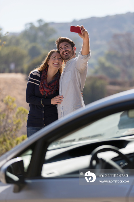 Happy couple taking selfie outside car at sunny roadside