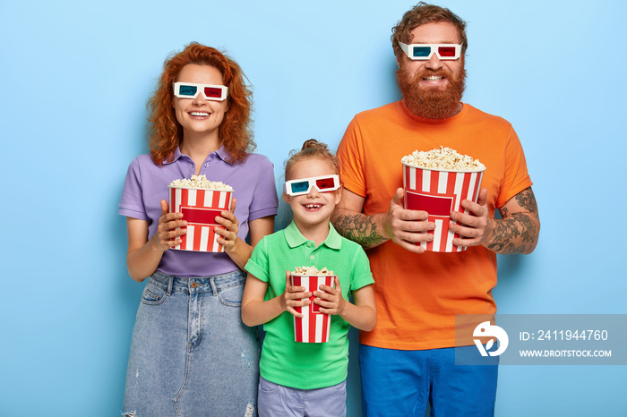 Family time. Joyful redhead mother, father and little daughter have positive smiles, wear 3d glasses