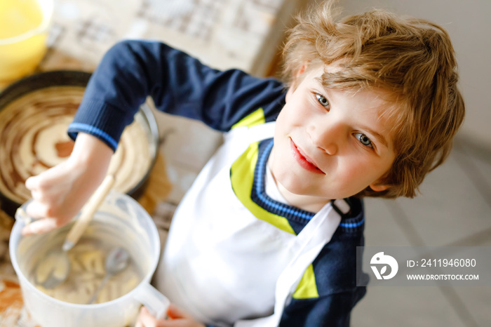 Adorable funny blond little kid boy baking chocolate cake and tasting dough in domestic kitchen, ind