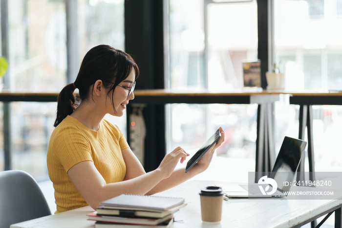 woman using laptop and tablet while relishing coffee at white desk in contemporary office