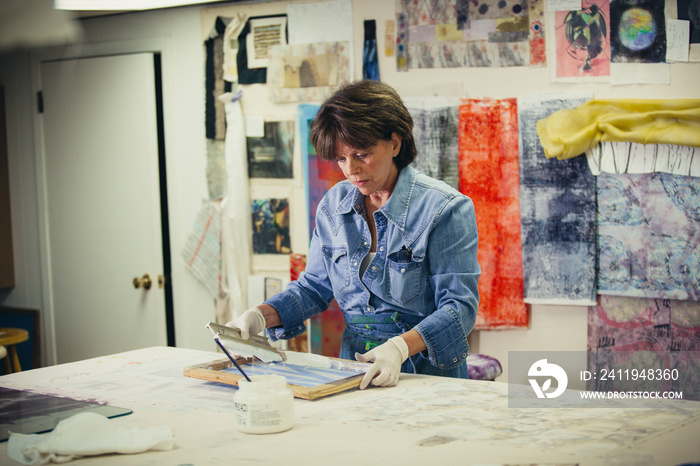 Focused craftswoman using silk screen while working at workshop