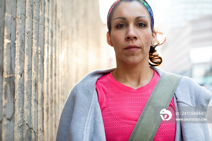 Portrait of serious female athlete standing by wall in city