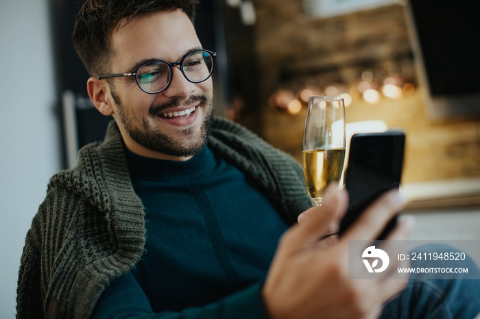 Happy man drinking Champagne while making video call over smart phone at home.