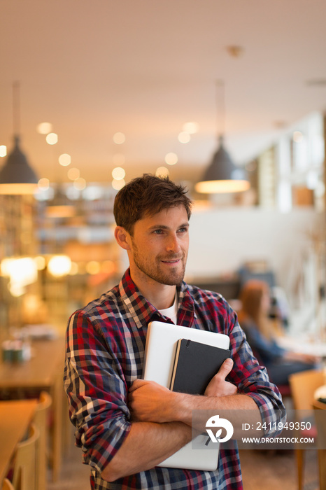 Man holding laptop and journal in cafe