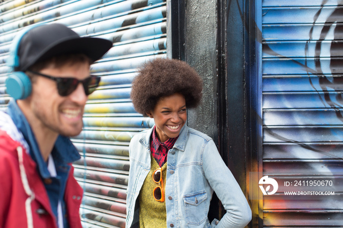 Happy young man and woman laughing against graffiti wall