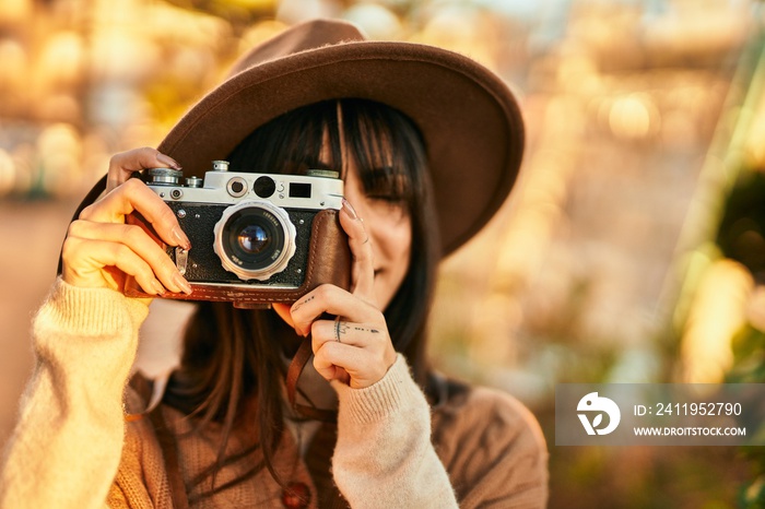 Brunette woman wearing winter hat smiling using vintage camera at the park